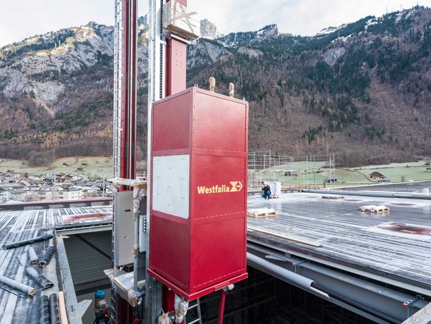 Ein Regalbediengerät wird per Kran durch ein Hallendach in ein Hochregallager eingebracht, Läderach (Schweiz) AG