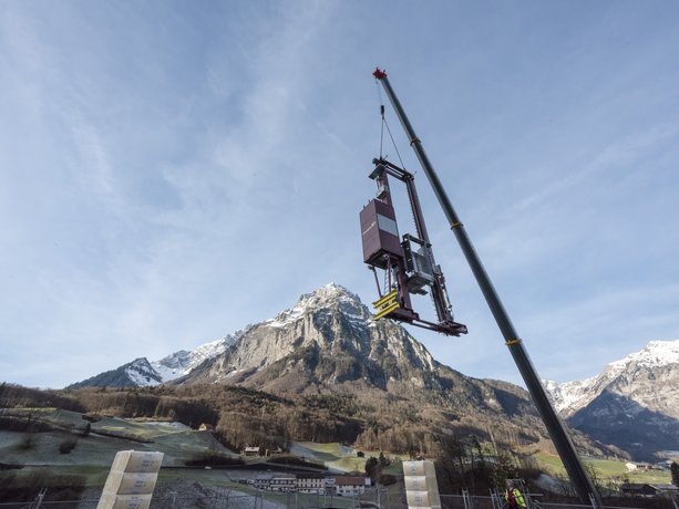 A storage and retrieval machine hovers on a crane above a high-bay warehouse in Switzerland, with mountains in the background